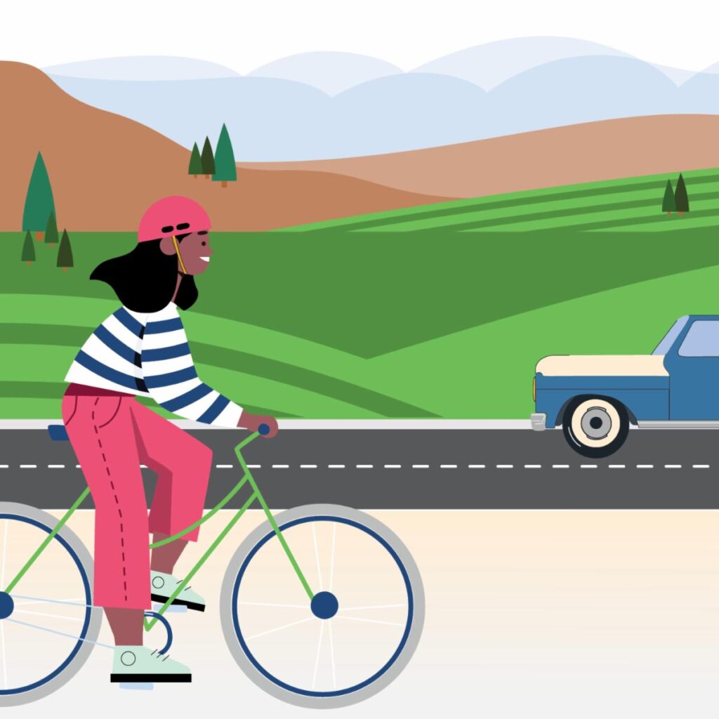 A person cycling on a road with hills and a parked car in the background.